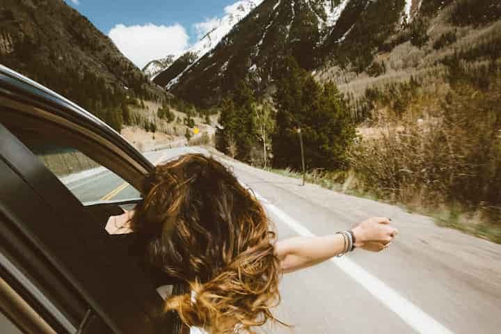 woman-riding-on-vehicle-putting-her-head-and-right-arm-outside-the-window-while-travelling-the-road-trip